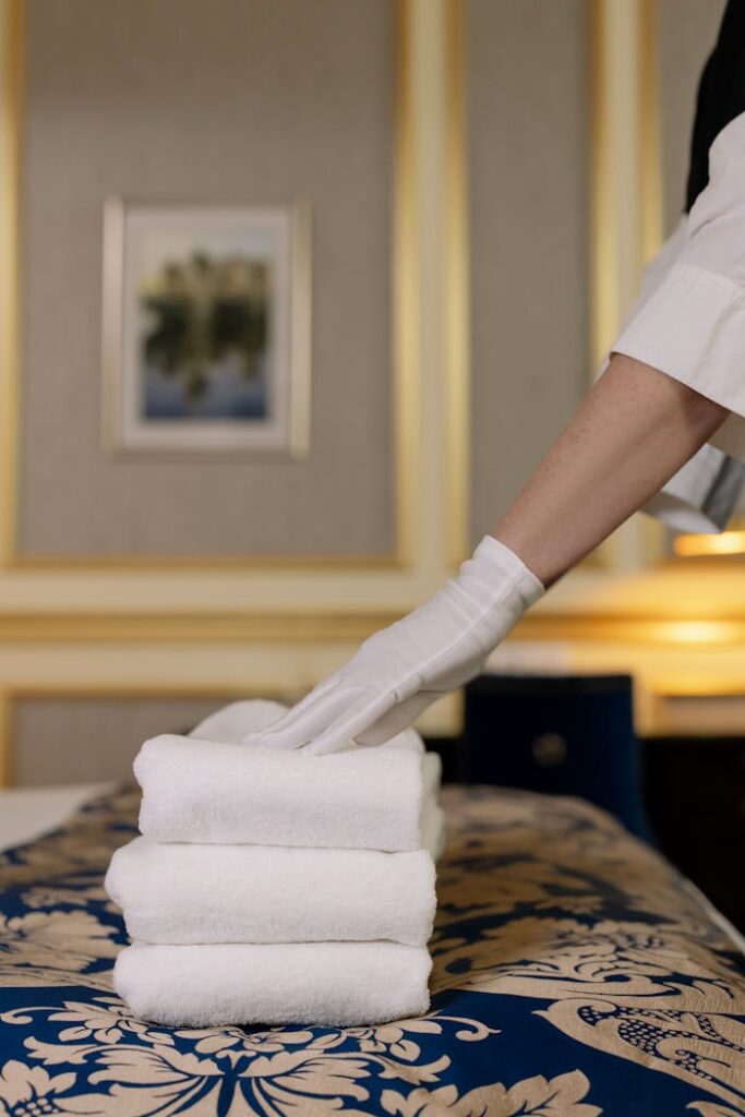 A hotel housekeeper in uniform arranges freshly laundered towels in a luxurious room.